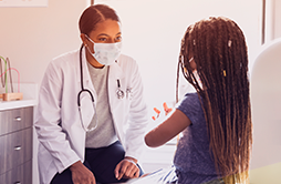 Médica pediatra de máscara conversando com criança